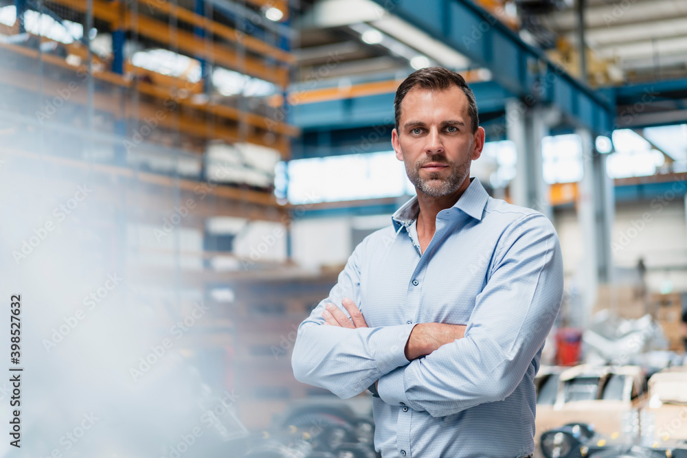 Male entrepreneur with arms crossed standing in industry Male entrepreneur with arms crossed standing in industry