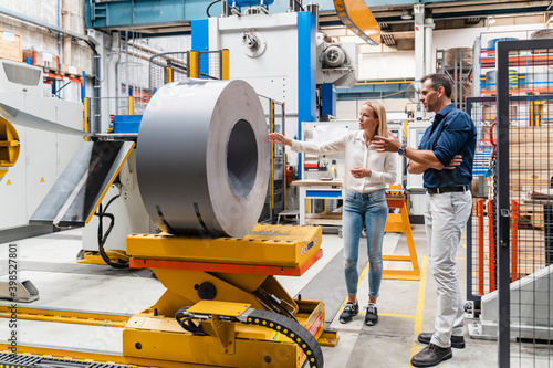 Female entrepreneur examining steel roll with male colleague while standing in factory photo