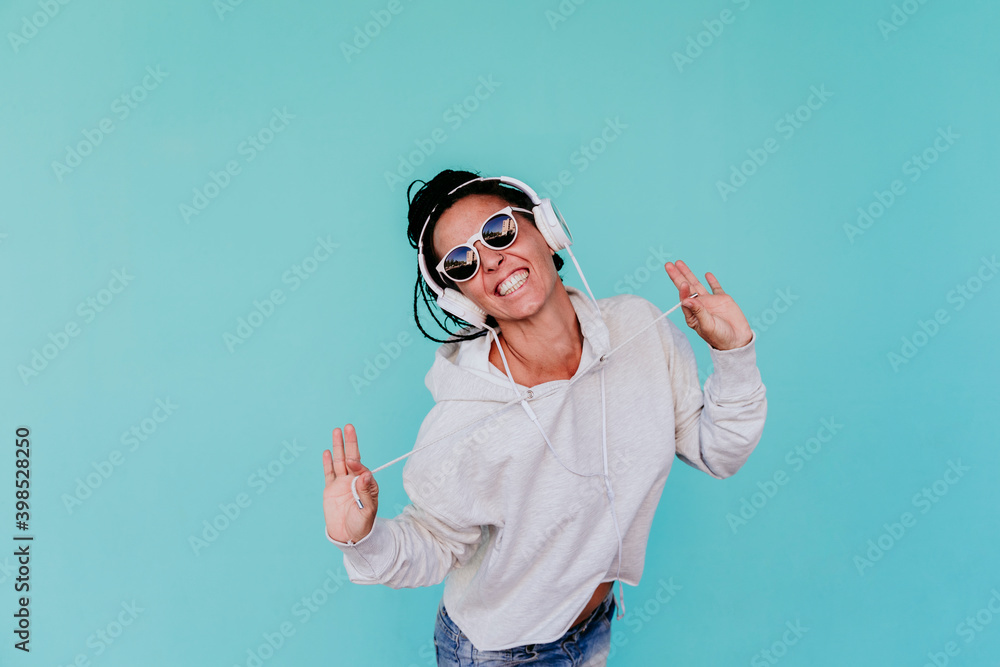 Cheerful woman listening music while pulling strings against turquoise background