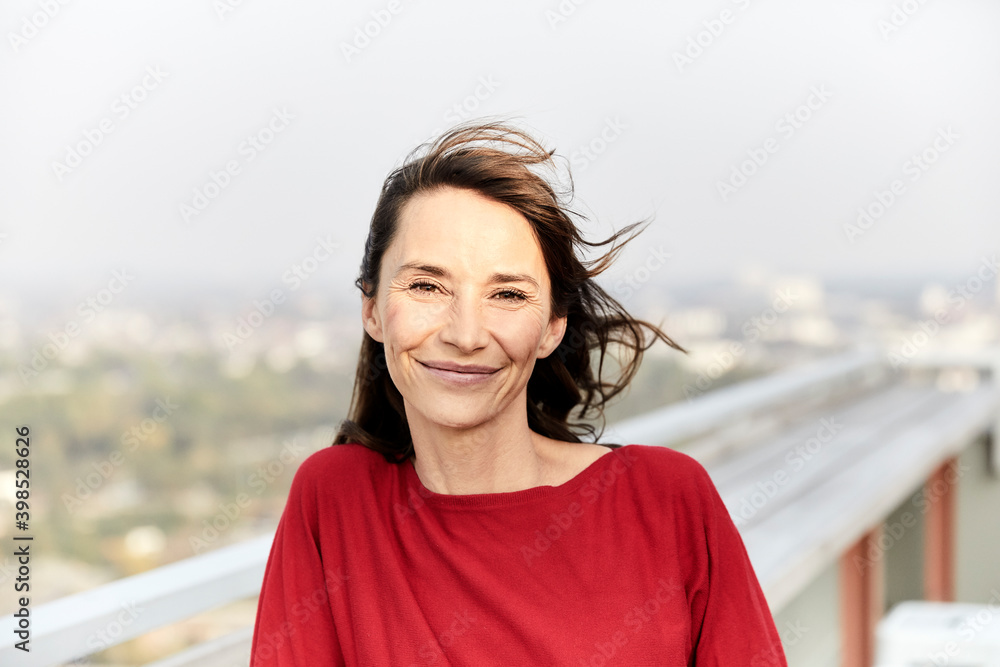 Smiling woman with hair blowing standing on building terrace Smiling woman with hair blowing standing on building terrace