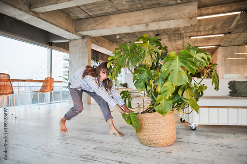 Mature woman pushing potted plant while standing at home