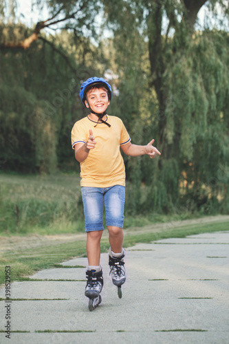 Happy smiling Caucasian preteen boy in helmet riding roller skates on road in park on summer day. Seasonal outdoors children activity sport. Healthy childhood lifestyle.