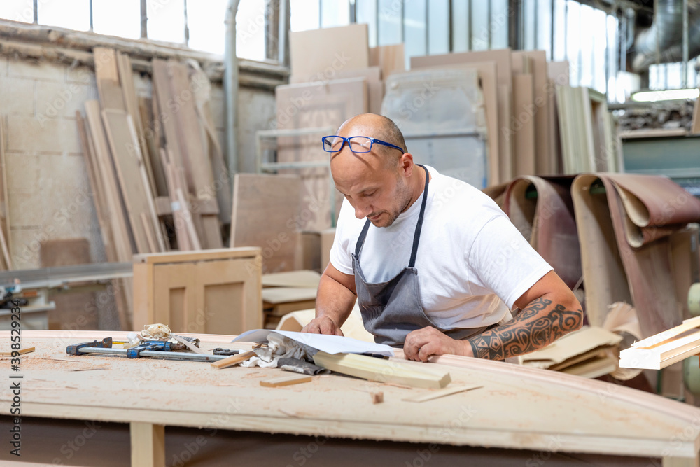 Carpenter reading design in paper while standing at workbench in factory Carpenter reading design in paper while standing at workbench in factory