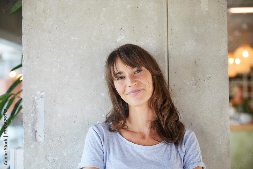 Smiling woman standing against concrete wall at home Smiling woman standing against concrete wall at home