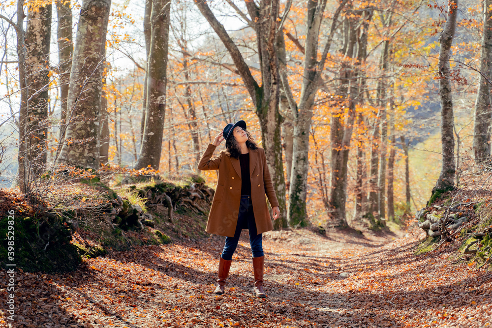 Woman wearing hat and jacket looking up while standing on footpath at forest Woman wearing hat and jacket looking up while standing on footpath at forest