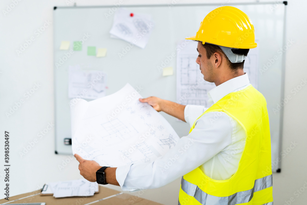 Young male architect examining blueprint at office Young male architect examining blueprint at office