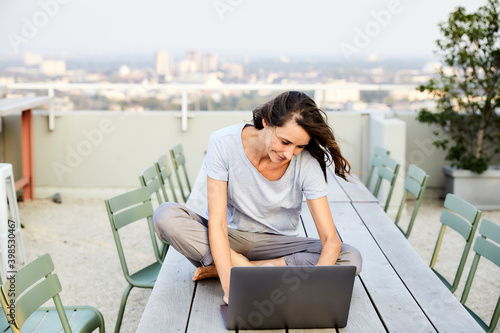 Mature woman with cross legged using laptop while sitting on building terrace