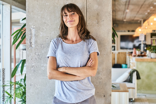 Confident woman standing with arms crossed against wall at home