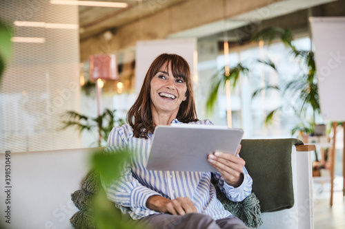 Happy woman using digital tablet while sitting at modern home