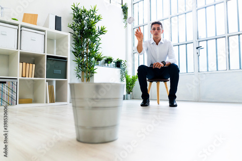 Bored male entrepreneur throwing crumpled paper ball in dustbin at office photo