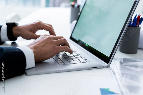 Hands of male professional tying on laptop keyboard at desk in workplace photo