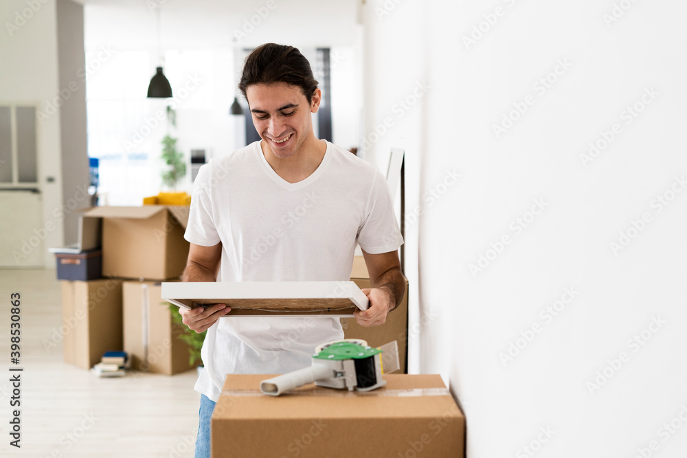 Smiling man looking at picture frame while reliving memories at new apartment Smiling man looking at picture frame while reliving memories at new apartment