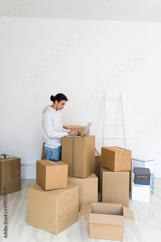 Young man using laptop by wall while shifting in new apartment