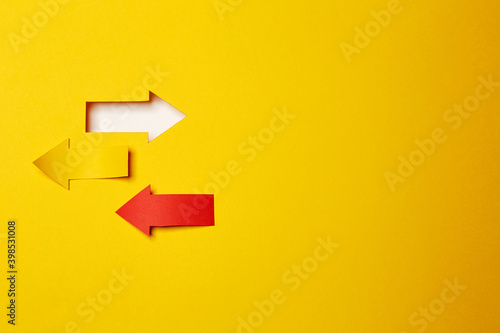 Three different direction left/right arrows, cutted from the yellow and red paper on the yellow paper background one made as an arrow shaped hole in the background with white paper underlay © Antonio
