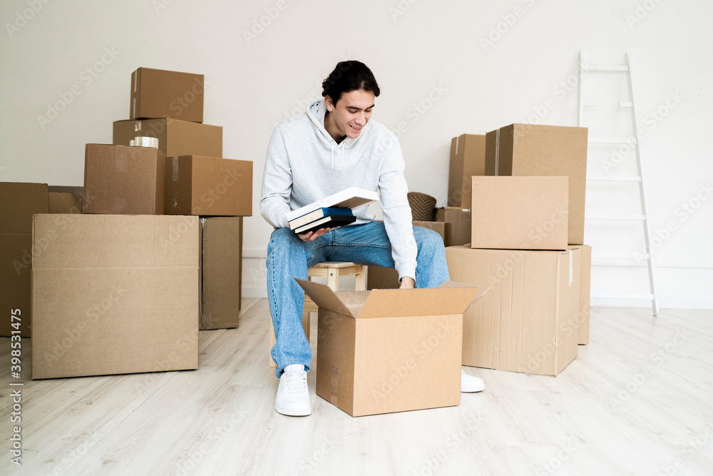 Young man removing books while unpacking box in new house Young man removing books while unpacking box in new house