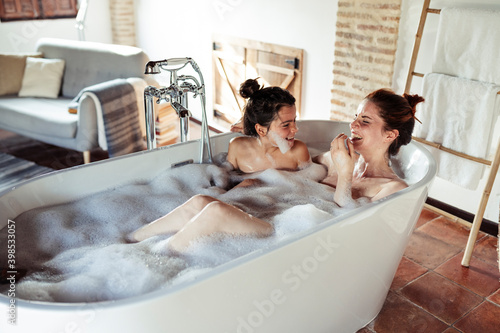 Smiling mother and daughter bathing in bathtub at home photo
