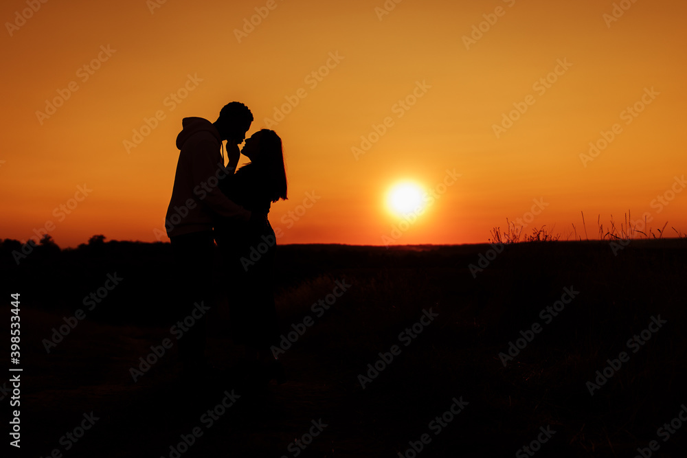 Silhouettes of lovely couple, handsome man gently hug beautiful woman at sunset, enjoy tender moments, caring husband and loving wife spend time together, weekends outdoors concept