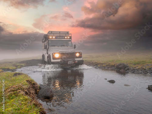 Off-road vehicle splashing water from puddle against cloudy sky at sunset photo