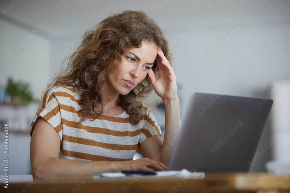 Woman sitting with head in hands while working on laptop at home Woman sitting with head in hands while working on laptop at home
