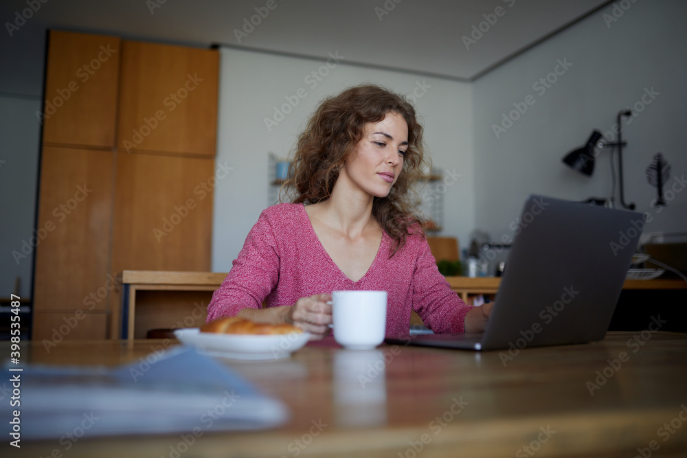 Woman having breakfast while working on laptop at home Woman having breakfast while working on laptop at home
