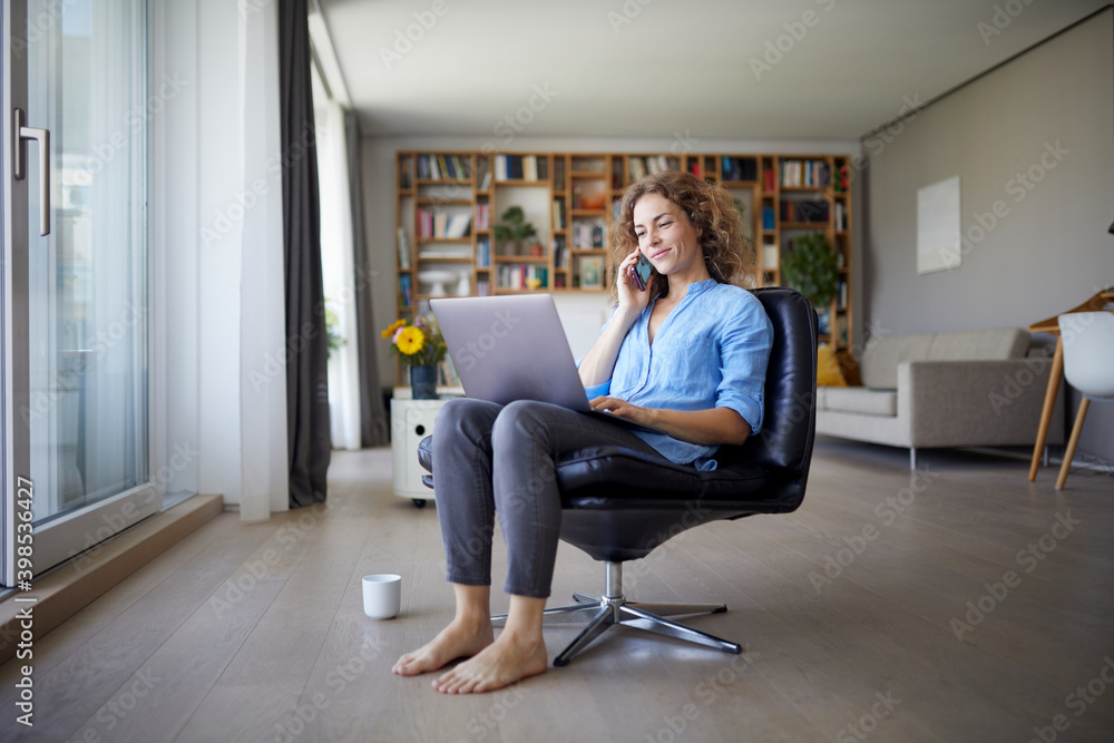 Woman talking on mobile phone while using laptop at home Woman talking on mobile phone while using laptop at home