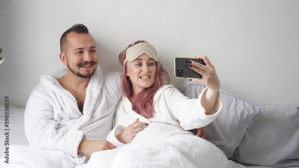 Couple on bed take photo on smartphone, adorable female hold mobile phone in hands, posing at camera, have rest. Couple on bed take photo on smartphone, adorable female hold mobile phone in hands, posing at camera, have rest.