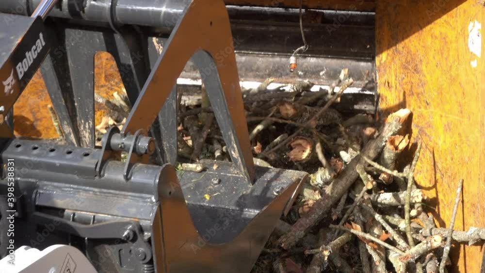 Close-up of a front-end loader pushing branches into the mouth of a wood chipper. Close-up of a front-end loader pushing branches into the mouth of a wood chipper.