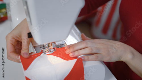 seamstress is stitching by sewing machine part of patchwork quilt, directing fabric under foot by hands