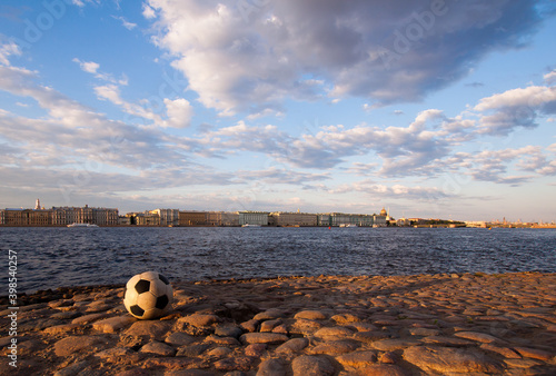 Deserted sunrise view of football (soccer ball) on paved embankment with morning cityscape background and blue cloudy sky. Peter and Paul Fortress, St.Petersburg, Russia.