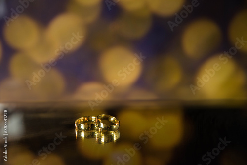 Golden wedding rings on sparkle bokeh background. Selective focus with copy space for text. Wedding card and invitation background. Champagne color. 