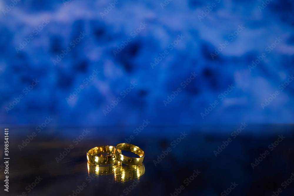 Golden wedding rings on sparkle bokeh background. Selective focus with copy space for text. Wedding card and invitation background. Blue color. Golden wedding rings on sparkle bokeh background. Selective focus with copy space for text. Wedding card and invitation background. Blue color.