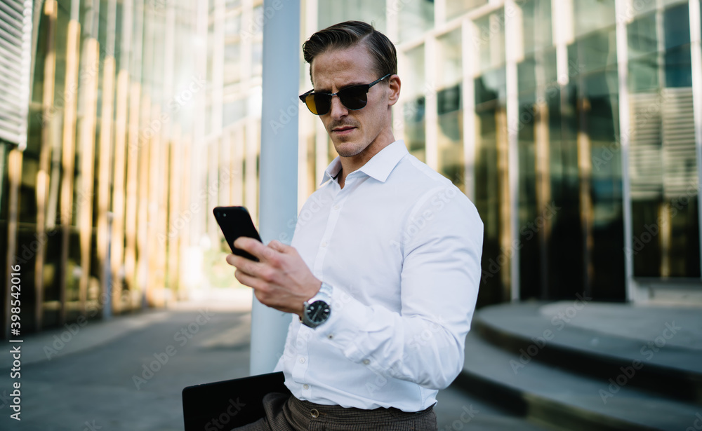 Serious businessman using smartphone near modern glass building