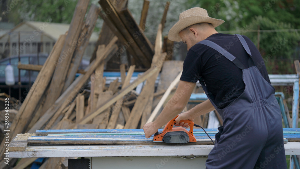 The man works as an electric bank. Processing old boards. Dealing with wood. The man works as an electric bank. Processing old boards. Dealing with wood.