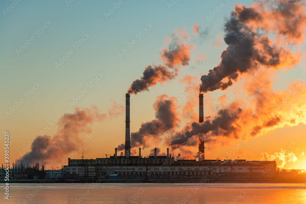 Smoke from chimney factory at sunrise. Pollution by industry smokestack against a red sunrise