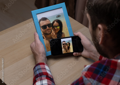 Canvas Print Man looking at photos in phone and in photo frame