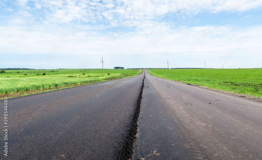 New asphalt road surface on the background of green and yellow fields to the horizon. The level of old and new asphalt. Highway on the background of a rural landscape. Horizontal line the roadside    