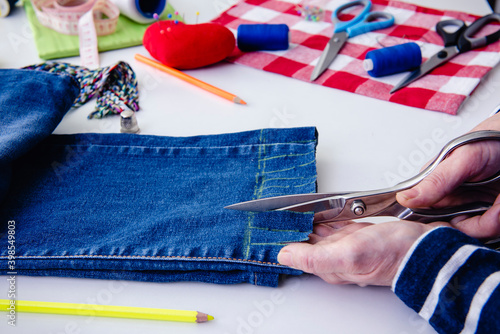 Manos de costurera con tijeras, cortando tiras de la parte inferior de los jeans photo
