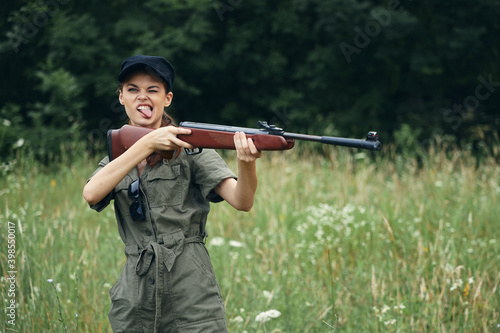 Military woman Shows his tongue with a weapon in his hands in a green jumpsuit black cap 