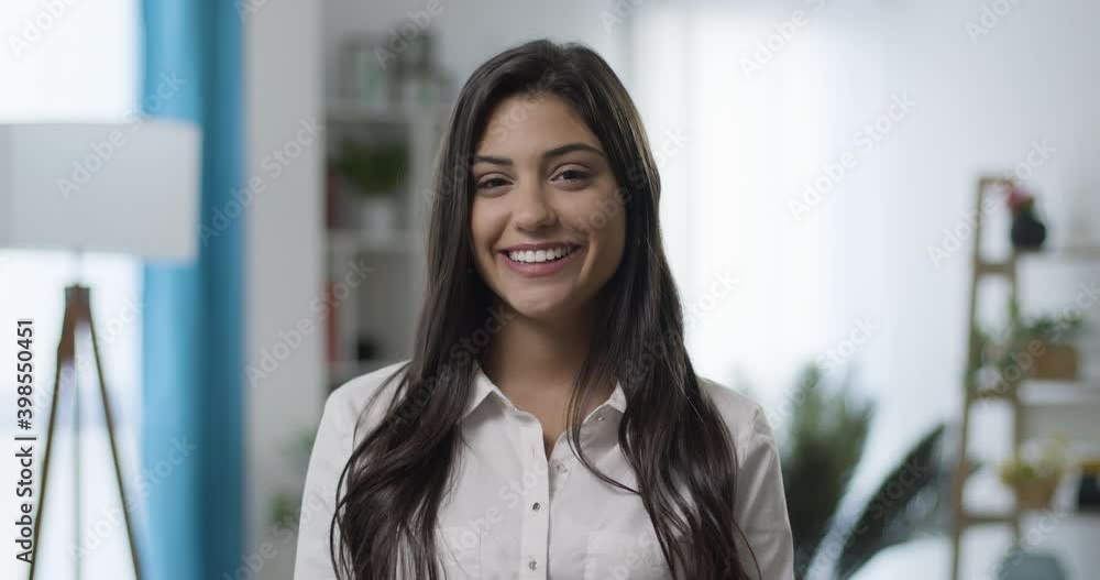 Slow motion of beautiful smiling confident young caucasian woman looking at camera smiling in living room or home office. Happy millennial authentic real girl close up portrait. Slow motion of beautiful smiling confident young caucasian woman looking at camera smiling in living room or home office. Happy millennial authentic real girl close up portrait.