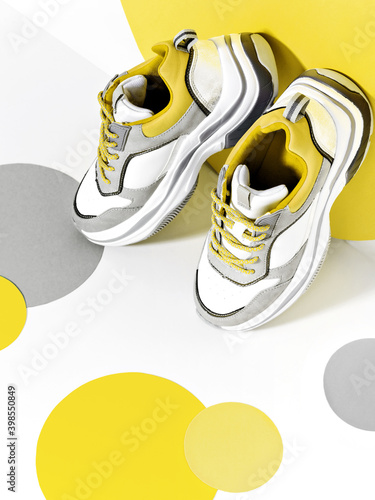 Bright scene with casual chunky sneakers and huge confetti in main colour of the year 2021. Illuminating and ultimate gray minimalist background. Sport and fitness idea.