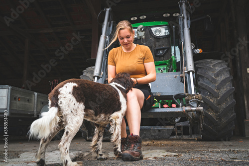 Hof- und Jagdhunde -junge Landwirtin mit ihrem Hund vor einem Traktor, Symbolfoto. photo