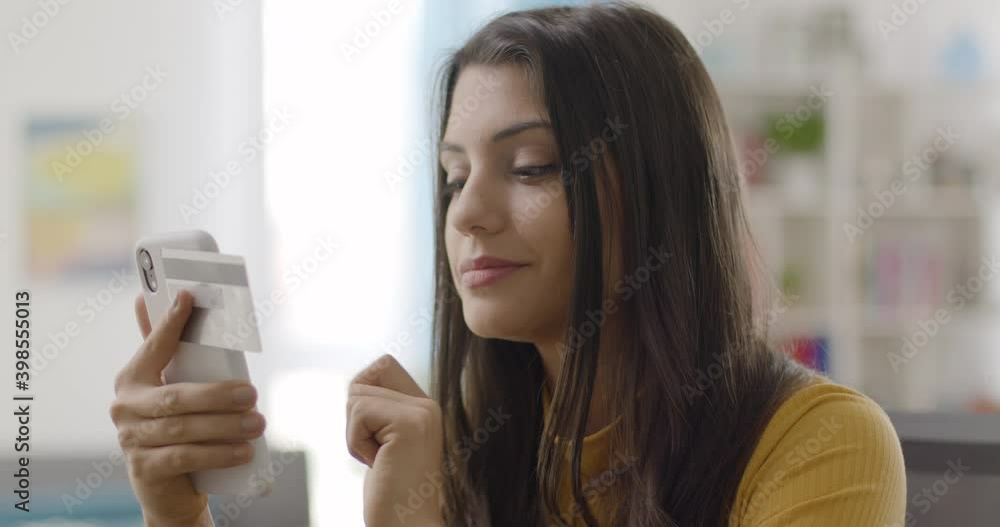 Close up slow motion of smiling young caucasian woman holding credit card and smartphone at home. Happy female shopper using mobile phone to make a purchase, online shopping. Close up slow motion of smiling young caucasian woman holding credit card and smartphone at home. Happy female shopper using mobile phone to make a purchase, online shopping.