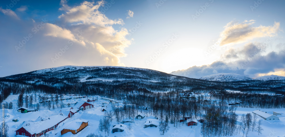 Scenic aerial panorama view on Tarna Vilt village in Joesjo lake area, Swedish Lapland in winter cover, frosty sunny day. Mountain cabins, birch trees with Scandinavian mountains at background