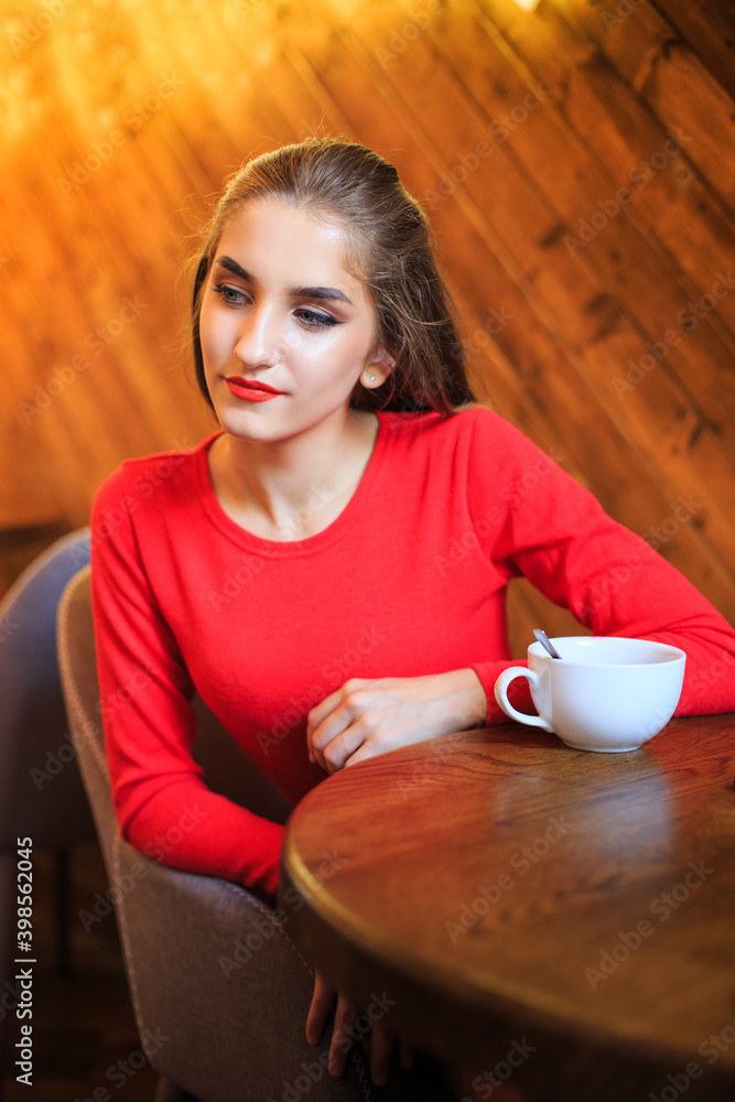 Young blue-eyed woman in red at a table in a cafe with a wooden interior Young blue-eyed woman in red at a table in a cafe with a wooden interior