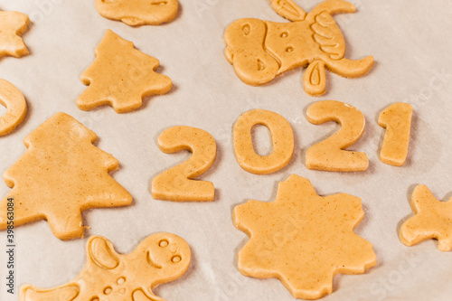 Woman hand cutting cookies, year 2021 on dark board with baking flour. rolling pin, flour and shape of new year figures.