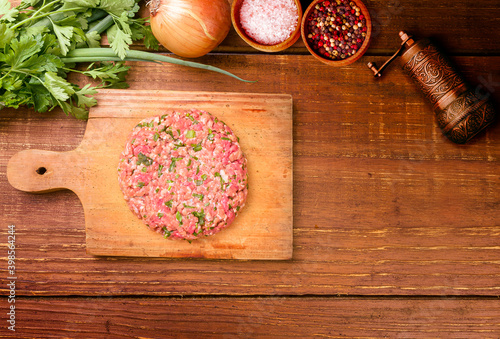 Fototapeta Naklejka Na Ścianę i Meble -  Raw minced meat with herbs and spices in a buger shape on a wooden board on a rustic wooden background.