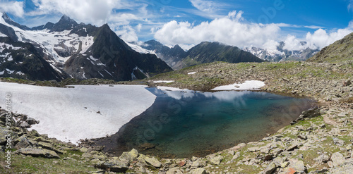 Fototapeta Naklejka Na Ścianę i Meble -  Panoramic view of glacial lake with springs from melting ice glacier with sharp snow-capped mountain peaks reflecting on water surface. Tyrol, Stubai Alps, Austria, summer sunny day