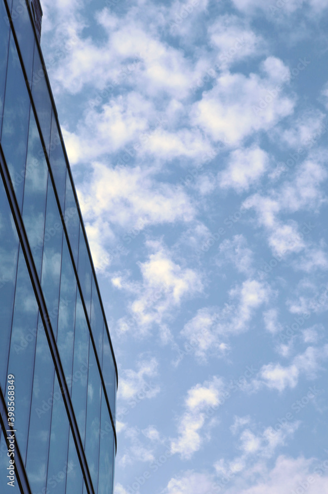 the corner of a modern glass office building next to a blue sky with white clouds the corner of a modern glass office building next to a blue sky with white clouds