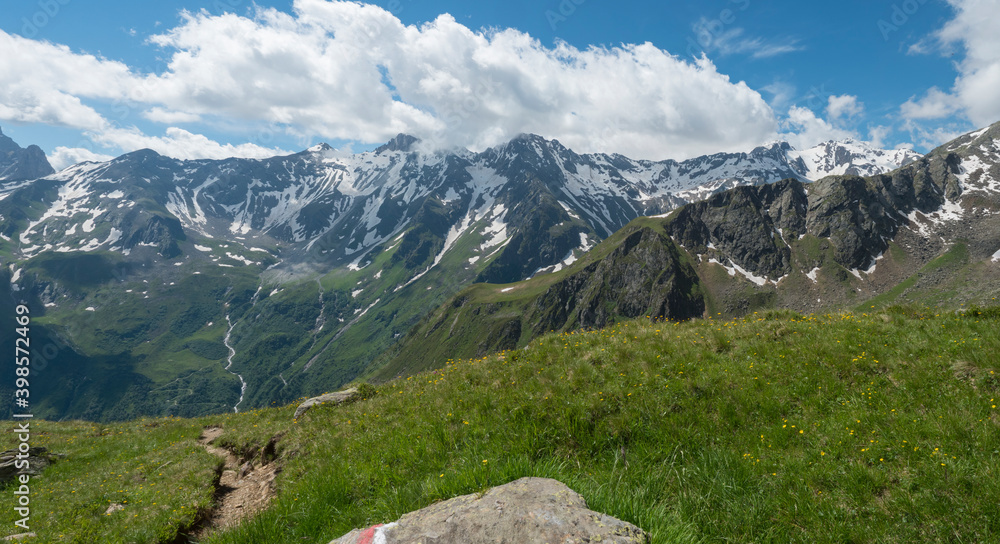 Panoramic view from Pramarnspitze saddle on snow-capped moutain panorama at Stubai hiking trail, Stubai Hohenweg, Alpine landscape of Tyrol Alps, Austria. Summer blue sky, white clouds