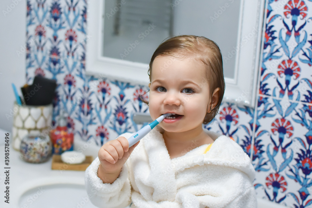 Naklejka premium Portrait of cute adorable baby girl or boy brushing teeth in bathroom with bright and white background. Beautiful child and morning dental hygiene in bath. Kids toothbrush concept. Healthy lifestyle.